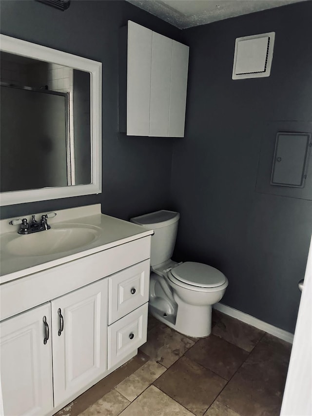 bathroom featuring vanity, a shower with shower door, toilet, and baseboards