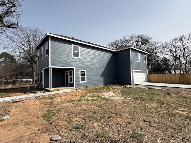 rear view of property with concrete driveway, an attached garage, and fence