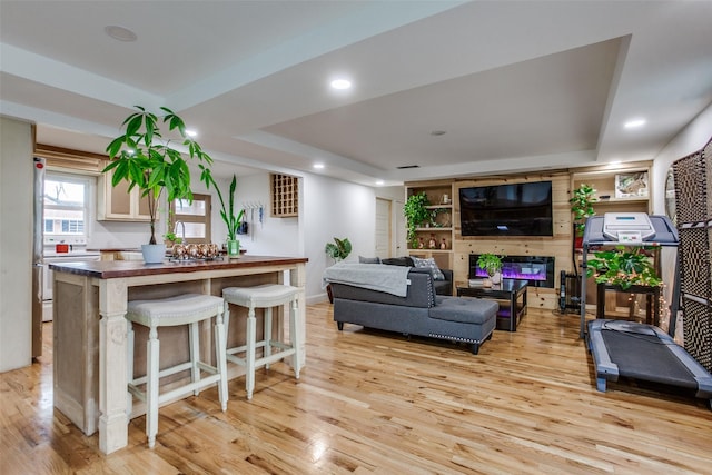 living area with recessed lighting, a raised ceiling, and light wood finished floors