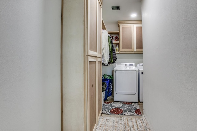 clothes washing area featuring cabinet space, a textured wall, and washing machine and clothes dryer