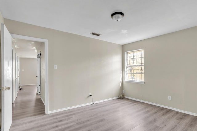 empty room with visible vents, light wood-type flooring, and baseboards