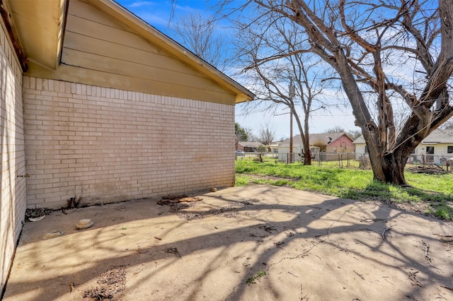 view of side of home featuring a patio, fence, and brick siding