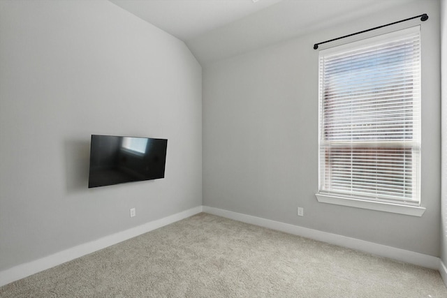 carpeted spare room featuring baseboards and vaulted ceiling