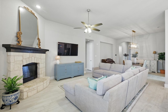 living area with arched walkways, a stone fireplace, wood finished floors, and a ceiling fan