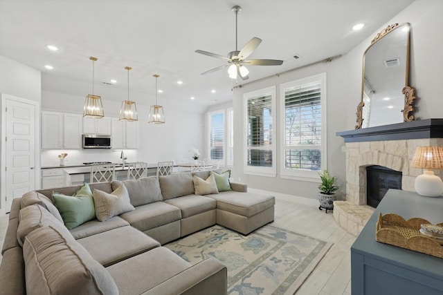 living room featuring light wood-type flooring, recessed lighting, a stone fireplace, baseboards, and ceiling fan