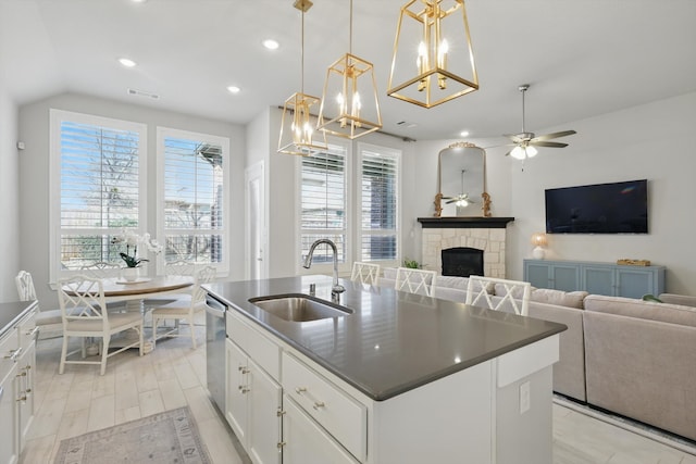 kitchen with a healthy amount of sunlight, a fireplace, a sink, stainless steel dishwasher, and dark countertops