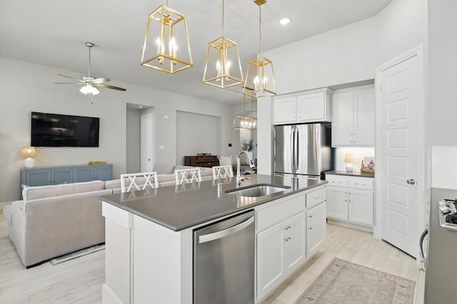 kitchen with a center island with sink, a sink, stainless steel appliances, dark countertops, and open floor plan