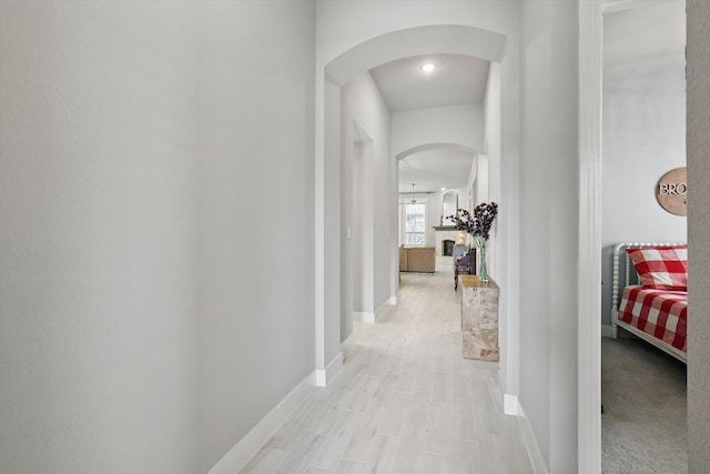 corridor featuring arched walkways, light wood finished floors, and baseboards