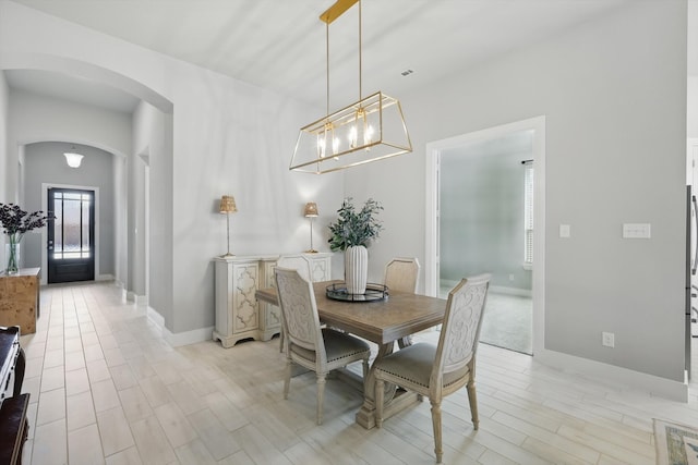 dining room featuring arched walkways, baseboards, and light wood-style floors