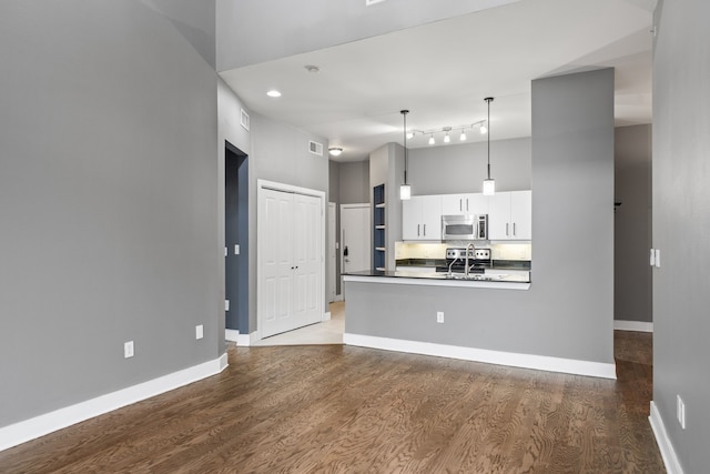 kitchen with white cabinetry, stainless steel microwave, dark countertops, and wood finished floors