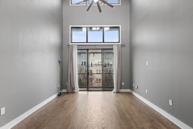 spare room with a ceiling fan, wood finished floors, baseboards, and a towering ceiling