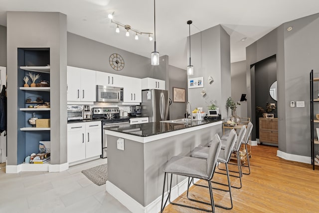 kitchen with dark countertops, white cabinets, a kitchen breakfast bar, and stainless steel appliances