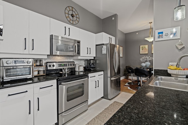 kitchen with decorative light fixtures, decorative backsplash, appliances with stainless steel finishes, white cabinets, and a sink