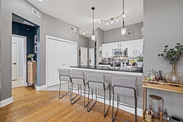 kitchen with dark countertops, white cabinetry, appliances with stainless steel finishes, a breakfast bar area, and a peninsula