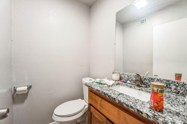 half bath featuring vanity, toilet, a textured wall, and visible vents