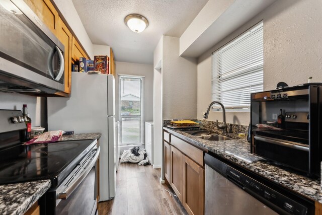 kitchen with a sink, appliances with stainless steel finishes, a textured ceiling, a textured wall, and light wood-type flooring