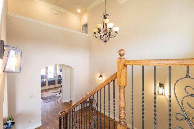 staircase with crown molding, baseboards, an inviting chandelier, wood finished floors, and arched walkways