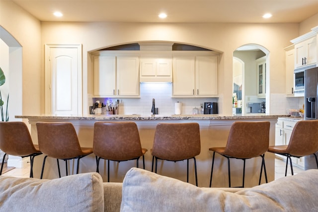 kitchen with light stone countertops, a breakfast bar, recessed lighting, white cabinetry, and backsplash