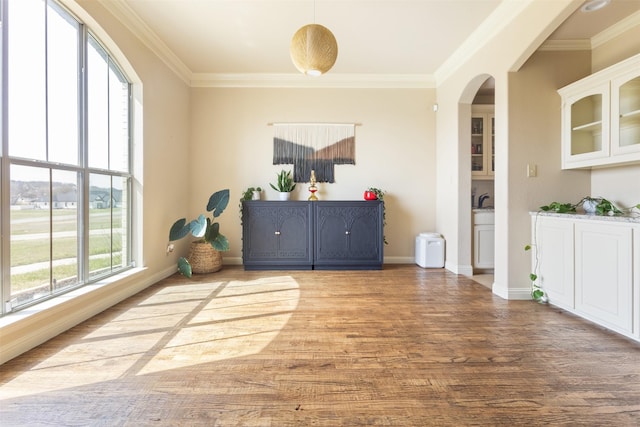 dining area featuring baseboards, arched walkways, wood finished floors, and crown molding