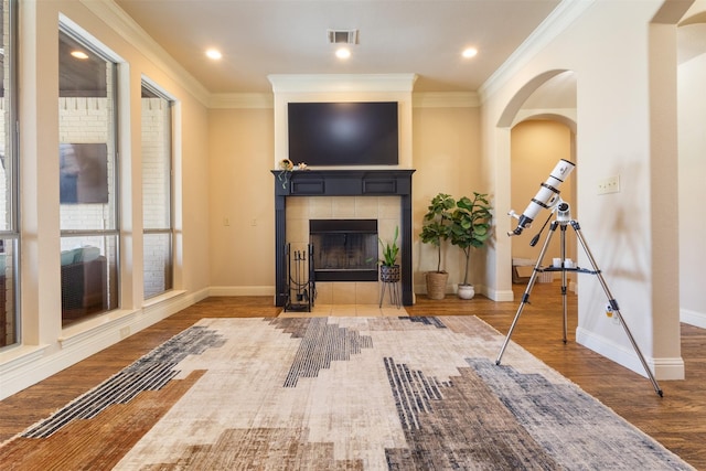 unfurnished living room with visible vents, baseboards, a tiled fireplace, ornamental molding, and wood finished floors