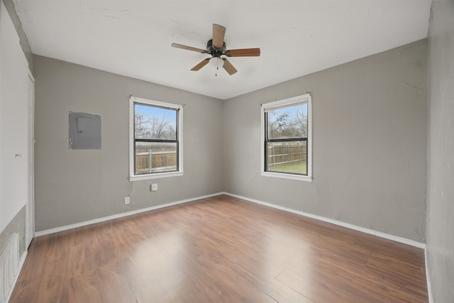 empty room with electric panel, baseboards, a healthy amount of sunlight, and wood finished floors