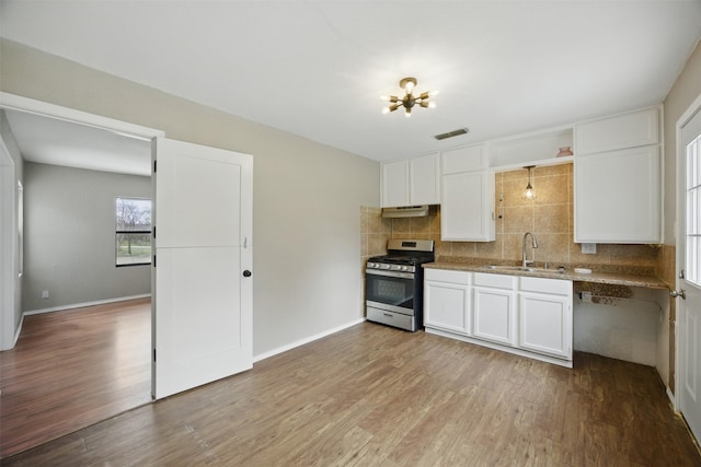 kitchen featuring wood finished floors, visible vents, stainless steel range with gas cooktop, a sink, and decorative backsplash