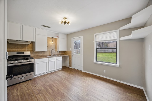 kitchen featuring tasteful backsplash, visible vents, under cabinet range hood, light wood-type flooring, and gas stove