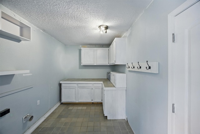 laundry room featuring cabinet space, a textured ceiling, and dark tile patterned flooring