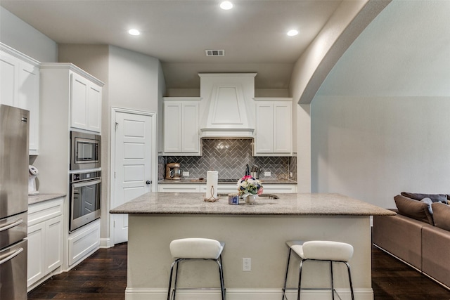 kitchen featuring premium range hood, visible vents, a kitchen breakfast bar, dark wood finished floors, and appliances with stainless steel finishes