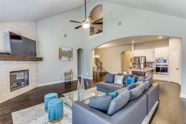 living area with visible vents, dark wood-style floors, arched walkways, a stone fireplace, and stairs