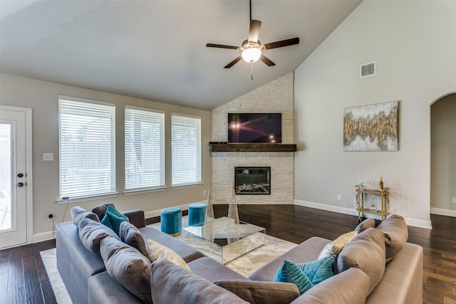 living area with wood finished floors, baseboards, visible vents, arched walkways, and a stone fireplace