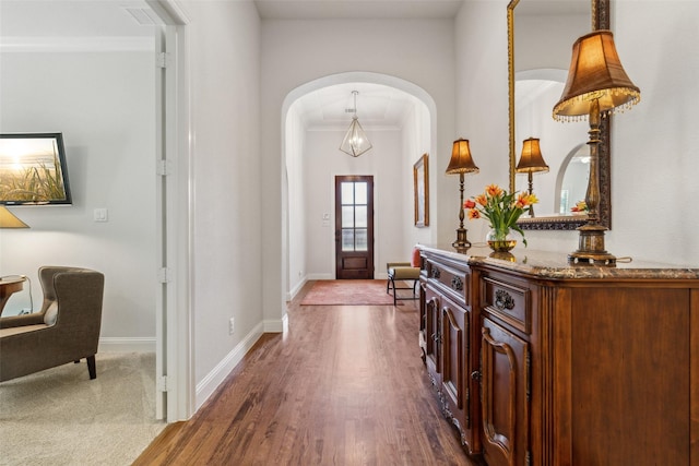 foyer with baseboards, arched walkways, wood finished floors, and crown molding