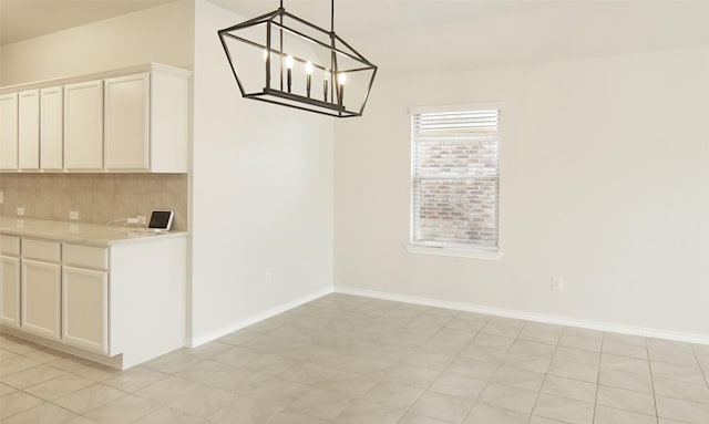 unfurnished dining area with an inviting chandelier and baseboards