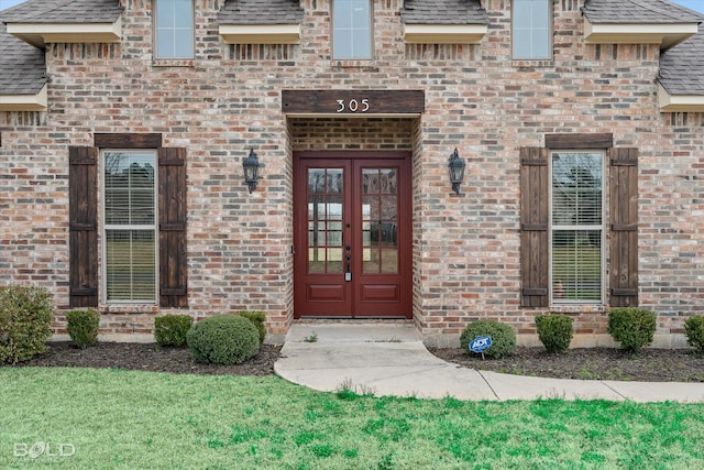 doorway to property featuring french doors, brick siding, and a shingled roof