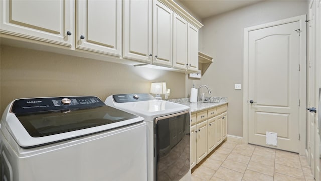 washroom with cabinet space, light tile patterned floors, washing machine and dryer, and a sink