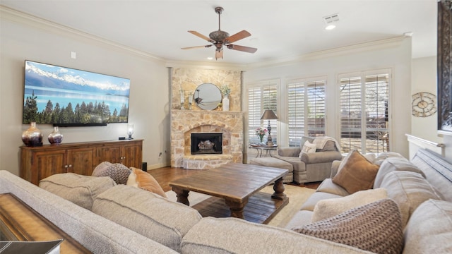 living room featuring visible vents, ceiling fan, ornamental molding, a stone fireplace, and wood finished floors