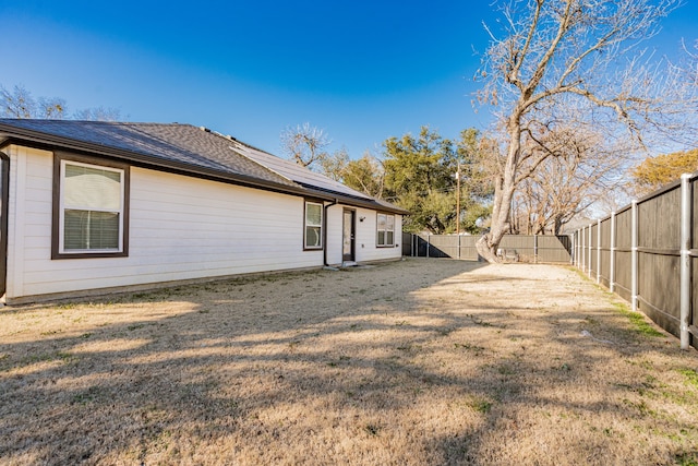 back of house featuring a yard, solar panels, a fenced backyard, and a shingled roof