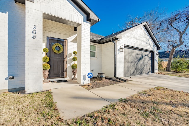 view of exterior entry featuring concrete driveway, brick siding, a garage, and a shingled roof