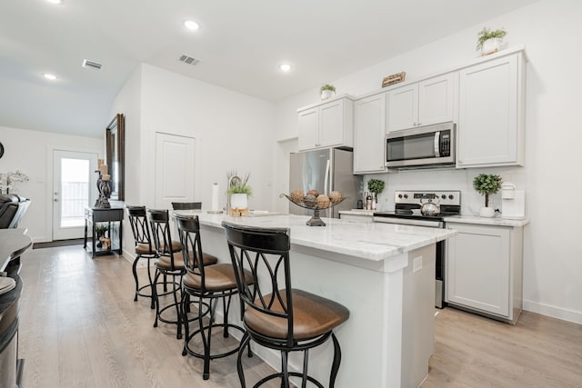 kitchen with visible vents, light wood-style floors, appliances with stainless steel finishes, a kitchen breakfast bar, and a center island