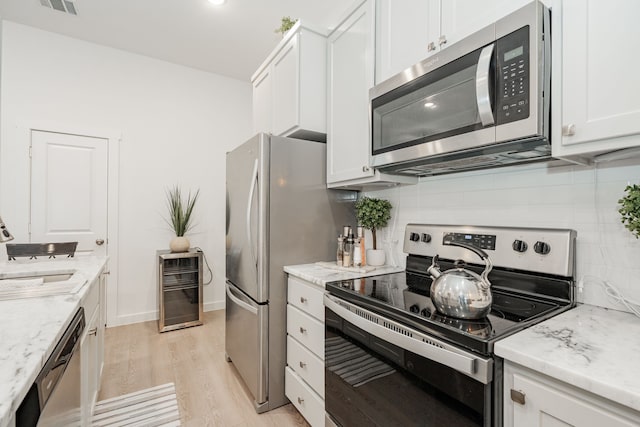 kitchen featuring decorative backsplash, appliances with stainless steel finishes, light wood-style floors, white cabinets, and a sink