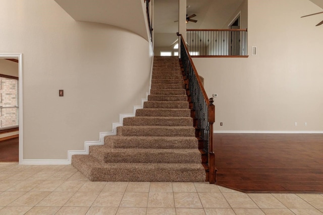 staircase with tile patterned floors, a ceiling fan, and a towering ceiling