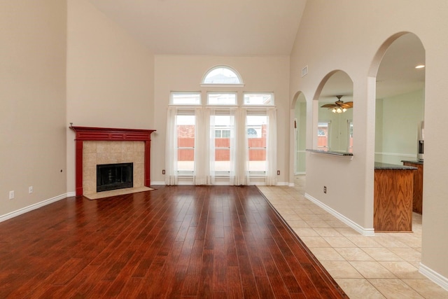 unfurnished living room featuring a high ceiling, baseboards, light wood finished floors, and a tile fireplace