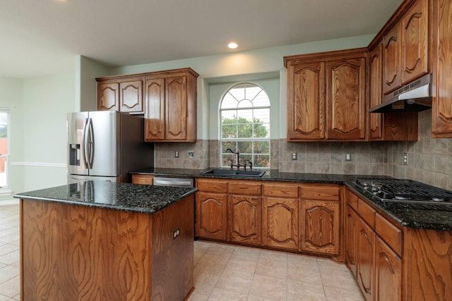 kitchen with dark stone countertops, a sink, stainless steel appliances, under cabinet range hood, and a center island