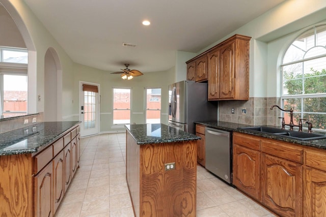 kitchen featuring a kitchen island, dark stone counters, a sink, appliances with stainless steel finishes, and backsplash