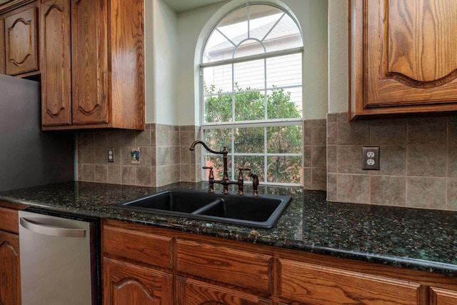 kitchen featuring a sink, decorative backsplash, dark stone countertops, brown cabinetry, and stainless steel dishwasher