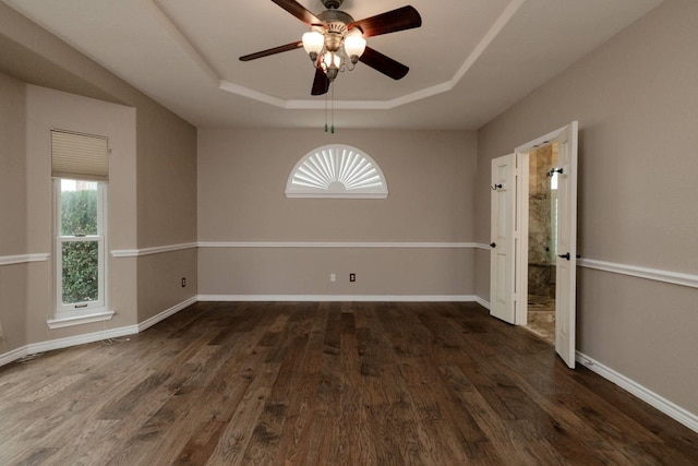 unfurnished dining area with ceiling fan, baseboards, a raised ceiling, and dark wood finished floors