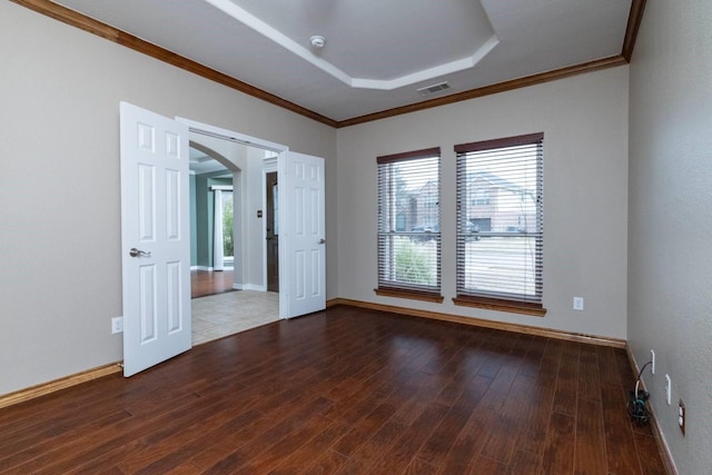 spare room featuring wood finished floors, visible vents, arched walkways, ornamental molding, and a raised ceiling