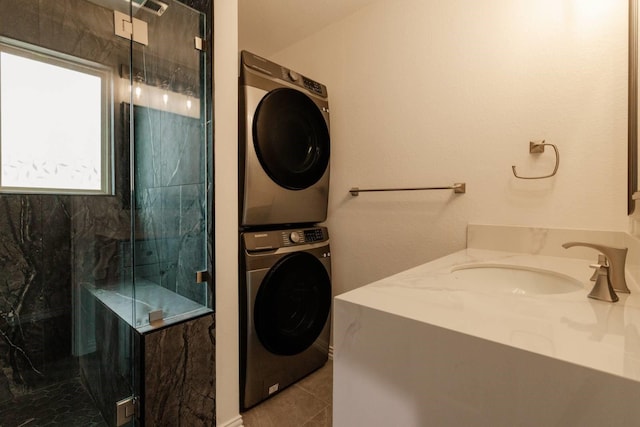 full bath featuring a marble finish shower, stacked washer and clothes dryer, vanity, and tile patterned flooring