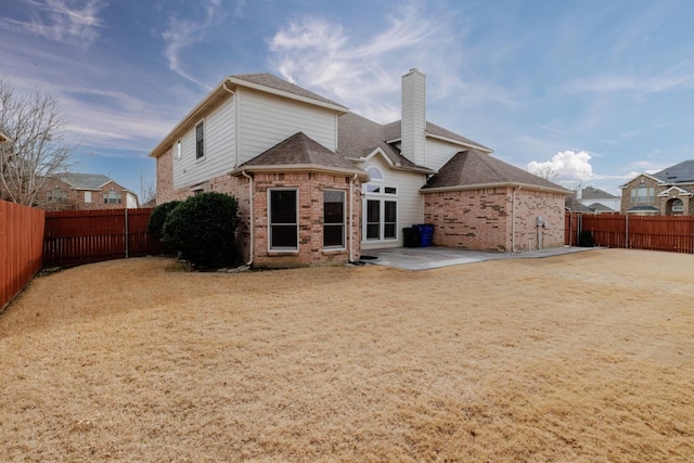 rear view of house with a fenced backyard, a shingled roof, brick siding, a chimney, and a patio area