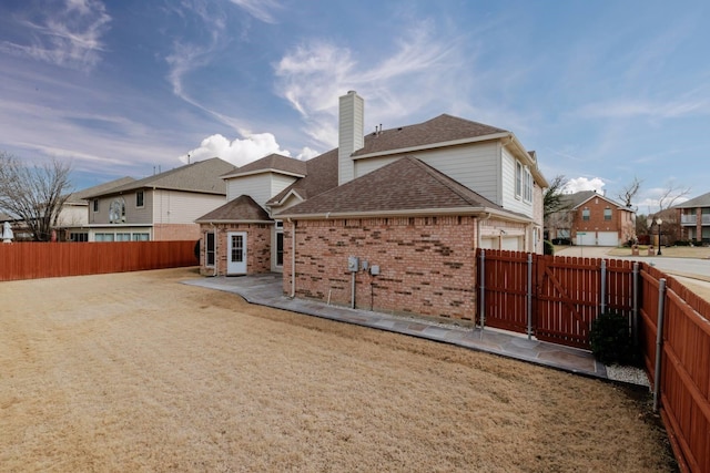 rear view of property with brick siding, a chimney, a fenced backyard, and roof with shingles